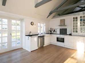 A modern kitchen with white cabinetry, a dishwasher, a stove, and a sink. There are large windows and a view of the outdoors.