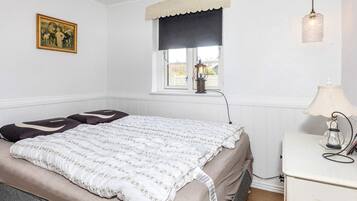 Et soveværelse med en seng, et vindue med sort gardin, en lampe og et billede på væggen.