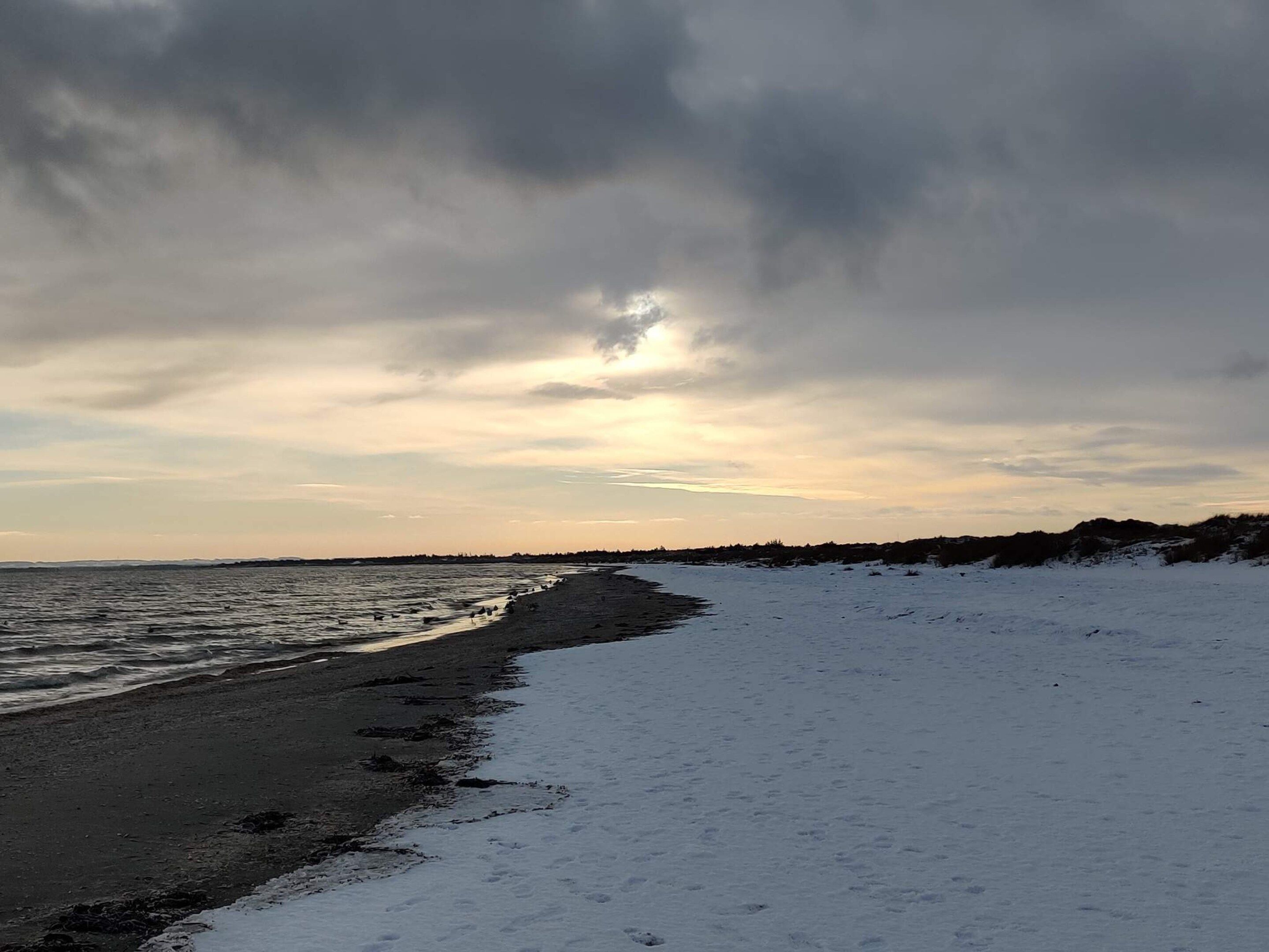 A beach with snow on the sand and a cloudy sky.