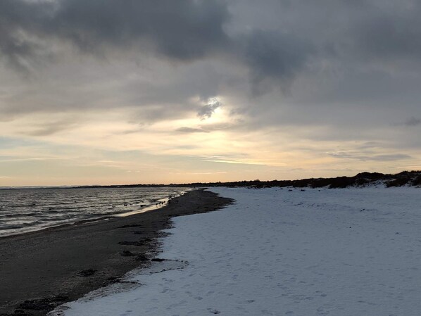 A beach with snow on the sand and a cloudy sky.