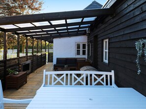 A covered outdoor deck with a wooden bench, a sofa, and a table. - 4 Star Holiday Home in Albaek (Aalbaek)