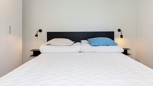 A double bed with a white quilt, two pillows (one beige, one blue), and two bedside lamps on either side.