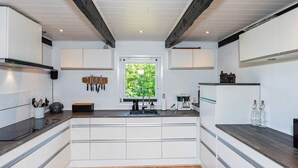 A modern kitchen with white cabinetry, a wooden countertop, and a window with a view of greenery.