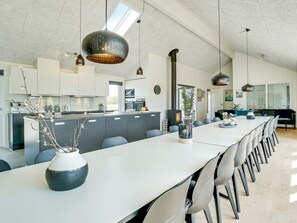 A modern kitchen with a central island, a dining area with a long table and chairs, and a large window providing natural light. - 5 Star Holiday Home in Grenaa (Grenaa)