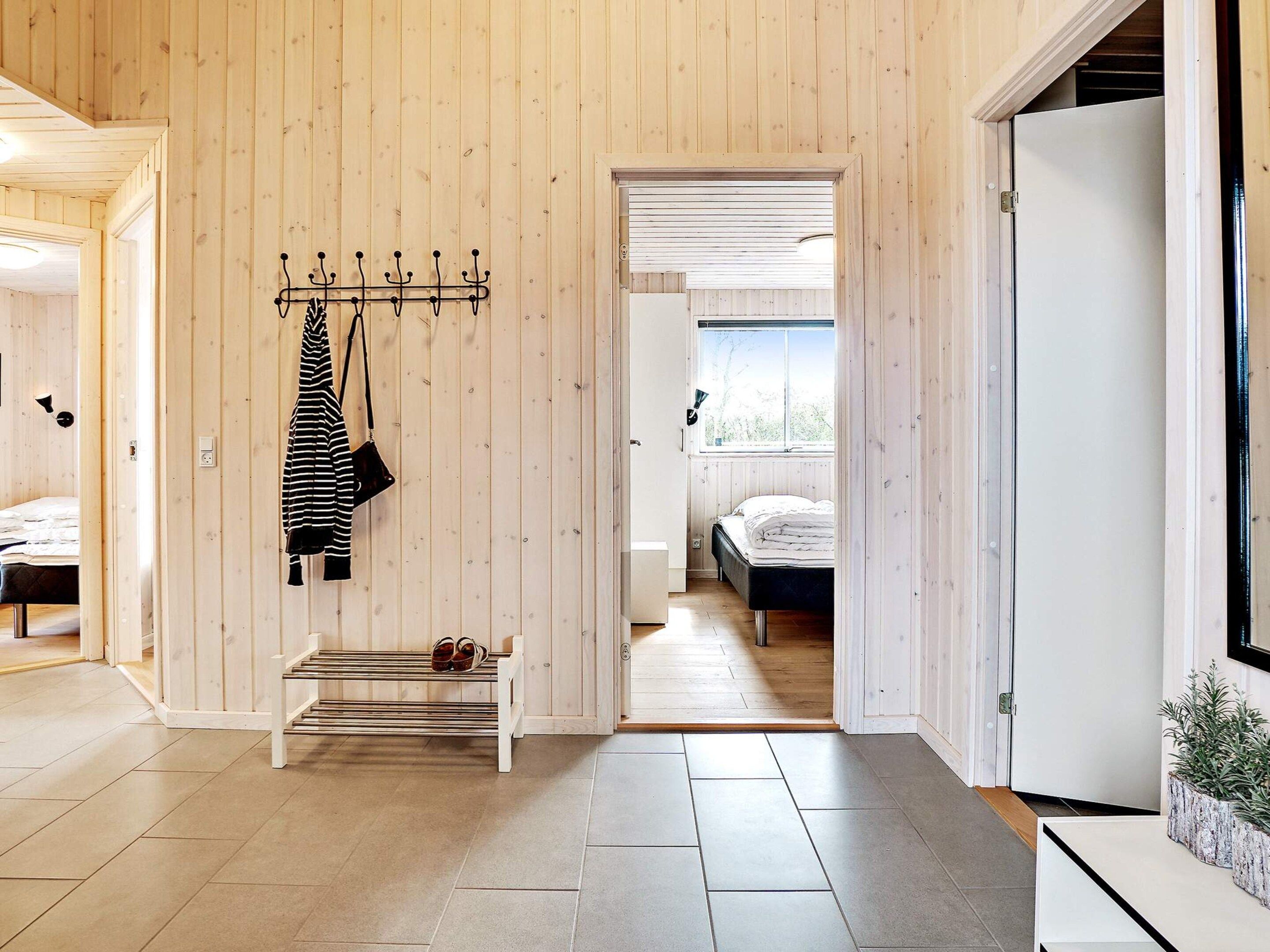 Un intérieur moderne avec un mur en bois, un banc, un porte-manteau et un lit dans la pièce adjacente.