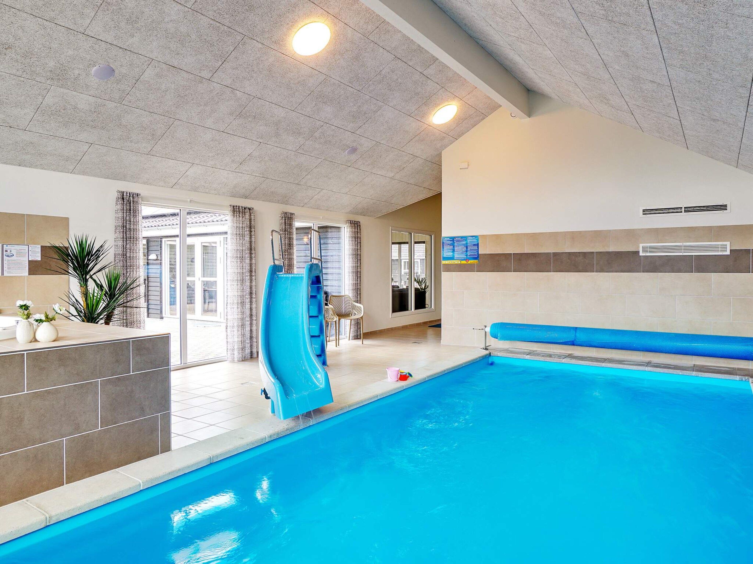 En indendørs swimmingpool med blå rutsjebane, siddeplads og udsigt ud