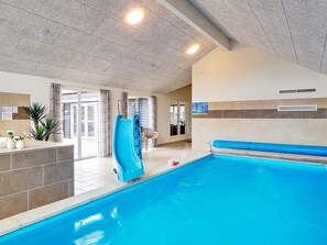 An indoor swimming pool with a blue slide, a seating area, and a view of the outside. - 5 Star Holiday Home in Grenaa (Grenaa)