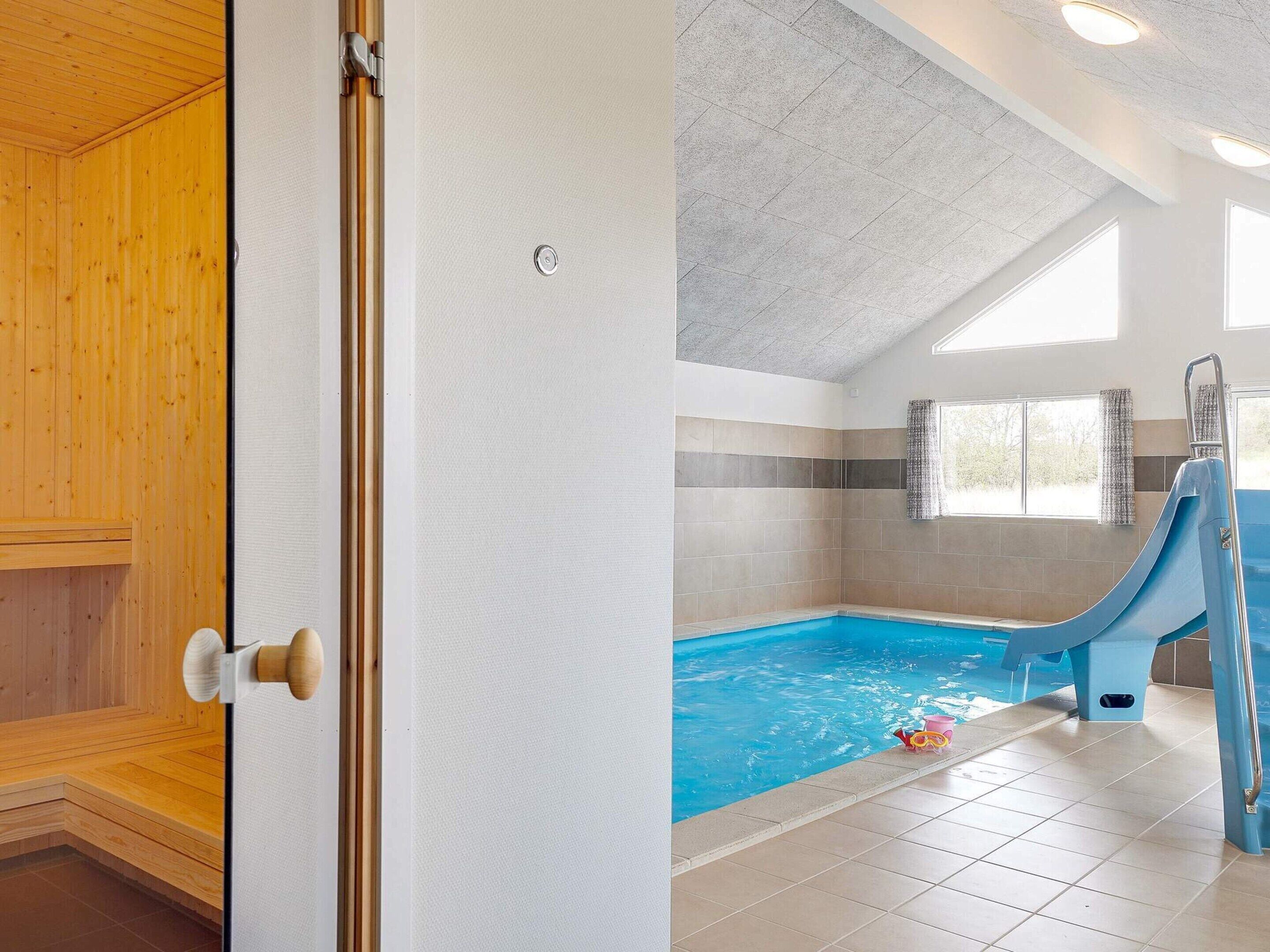 A room with a wooden door, a tiled wall, a pool with a blue slide, and a window with curtains.