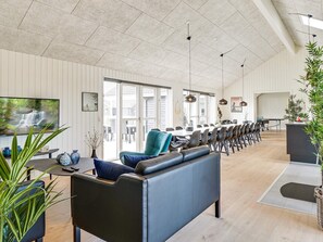 A spacious living area with a sofa, dining table, and chairs, a television, and a large window with a view of the outdoors. - 5 Star Holiday Home in Grenaa (Grenaa)