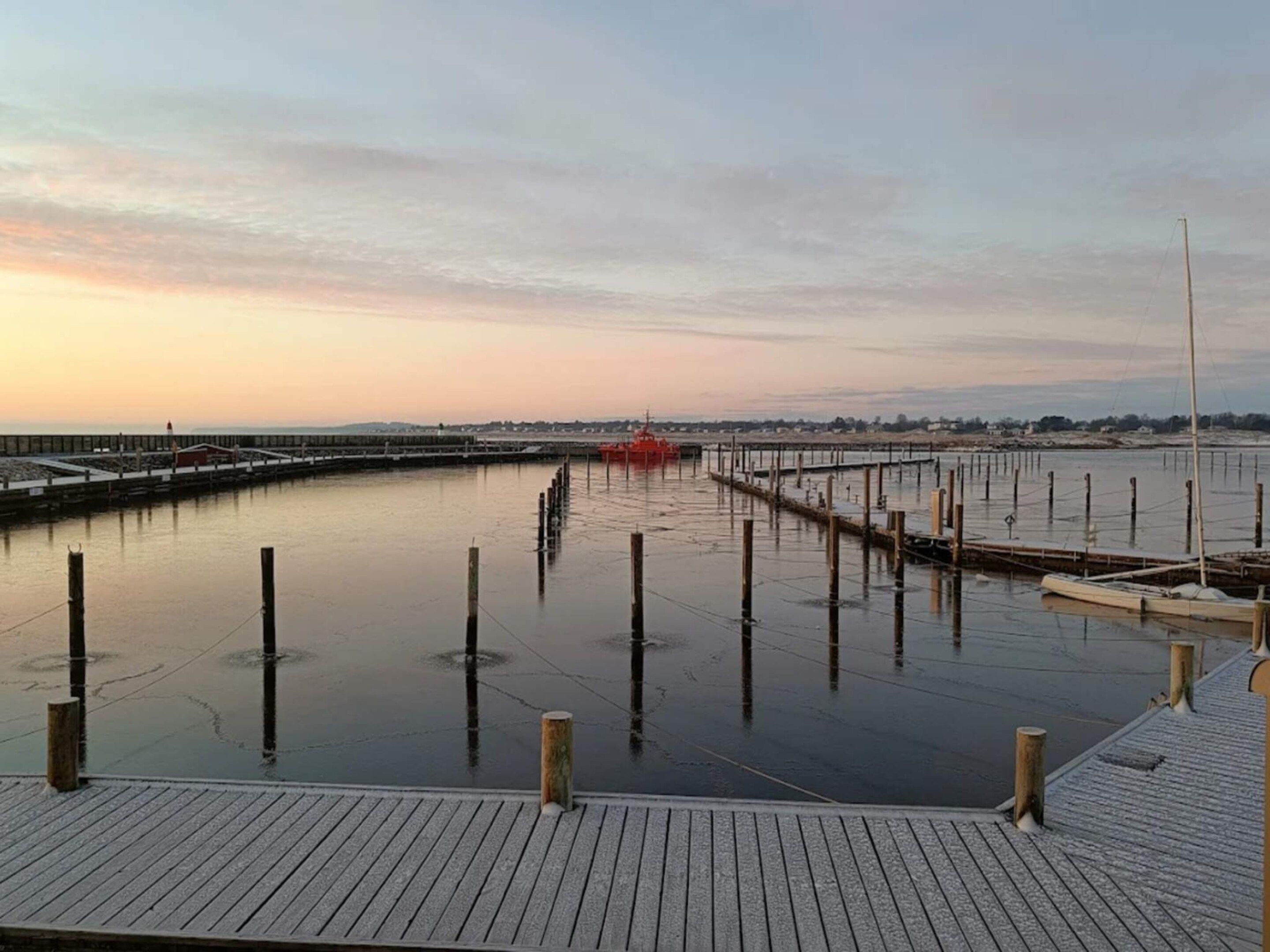 A waterfront pier with wooden posts and a red boat docked at the end.