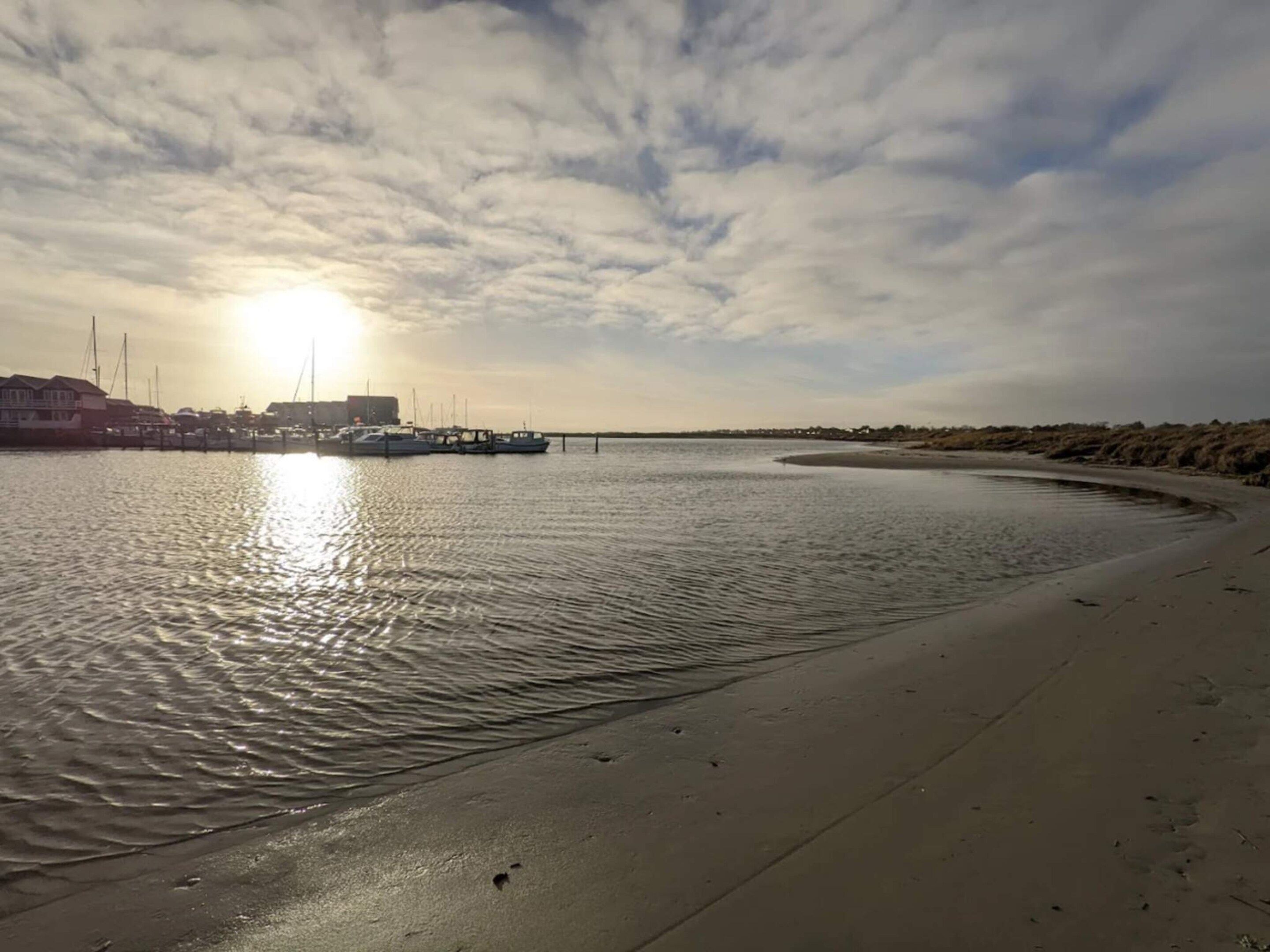 Et kystlandskab med et roligt vandareal, en sandstrand og en lysthavn med både.