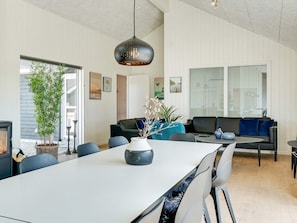 En moderne stue med spiseplads, der viser et stort bord, stole, en sofa og en hængende lampe.