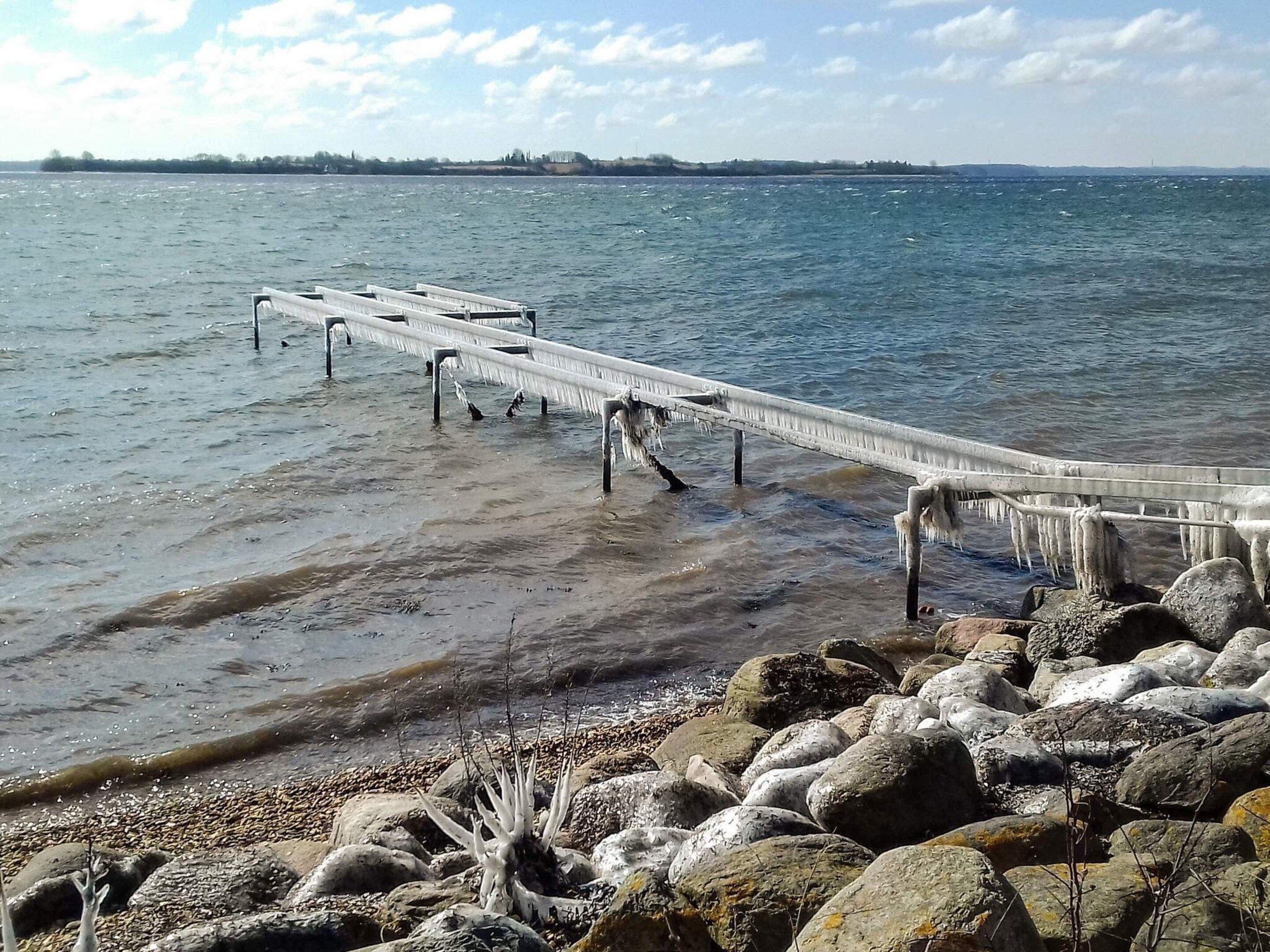 A pier extending into a body of water with a rocky shoreline in the foreground.