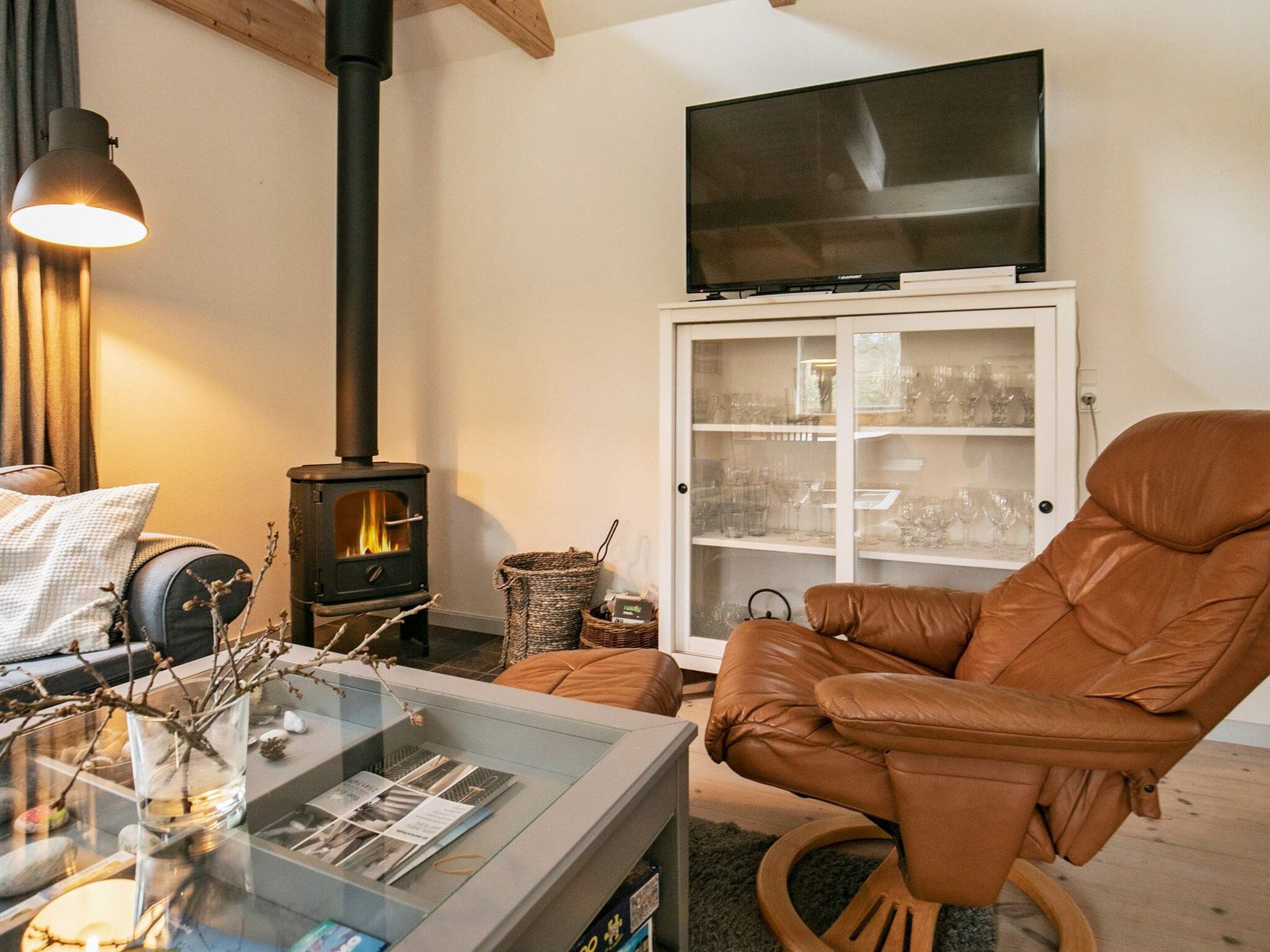A cozy living room with a fireplace, a comfortable leather chair, a glass coffee table, and a television on a cabinet.