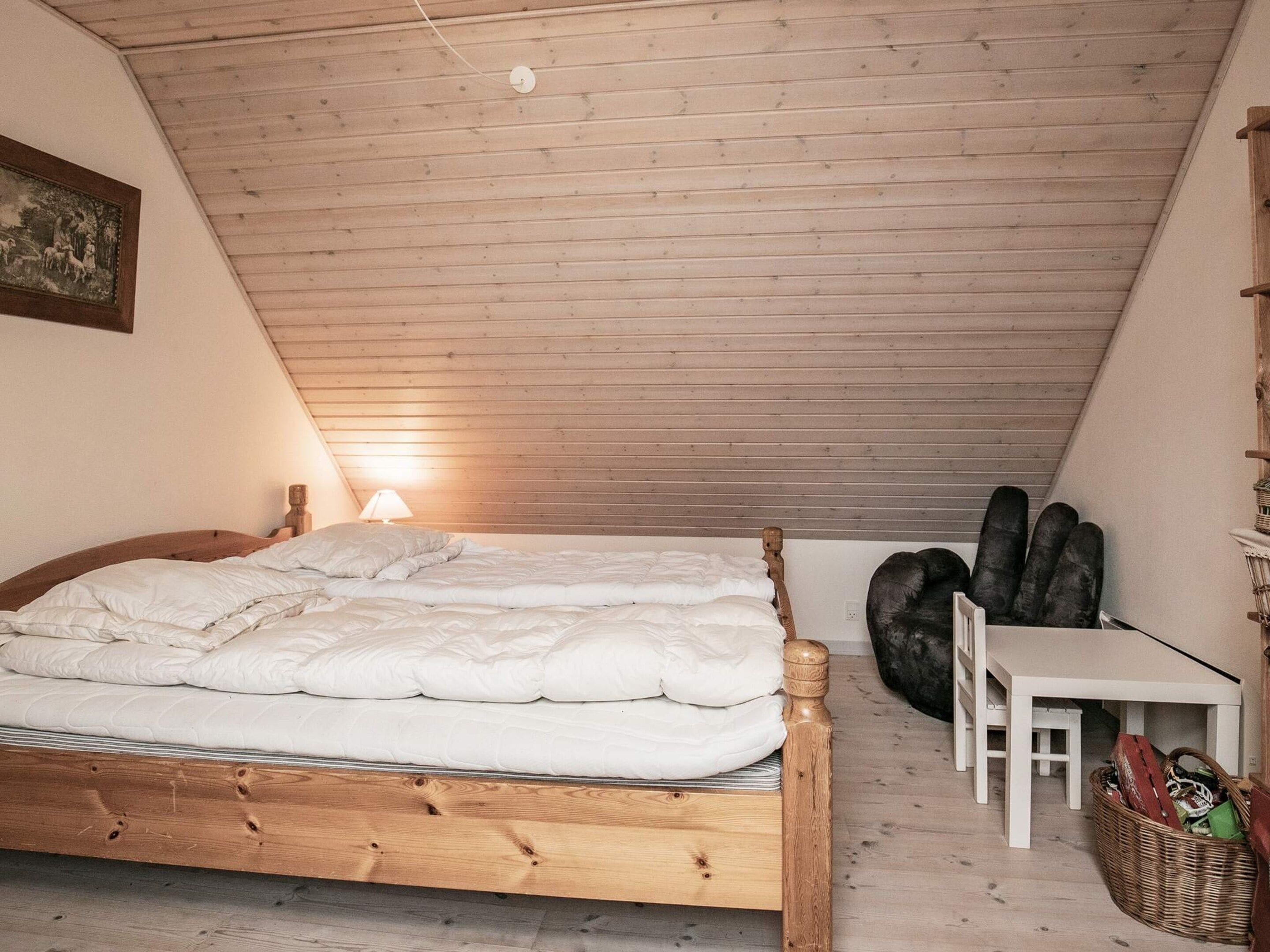 A bedroom with a wooden bed, a nightstand, a lamp, a small table, and a wicker basket.