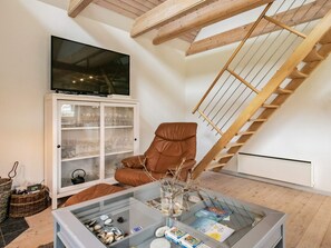 A loft bedroom with a glass coffee table, a brown leather chair, a white cabinet with glass doors, and a wooden staircase.