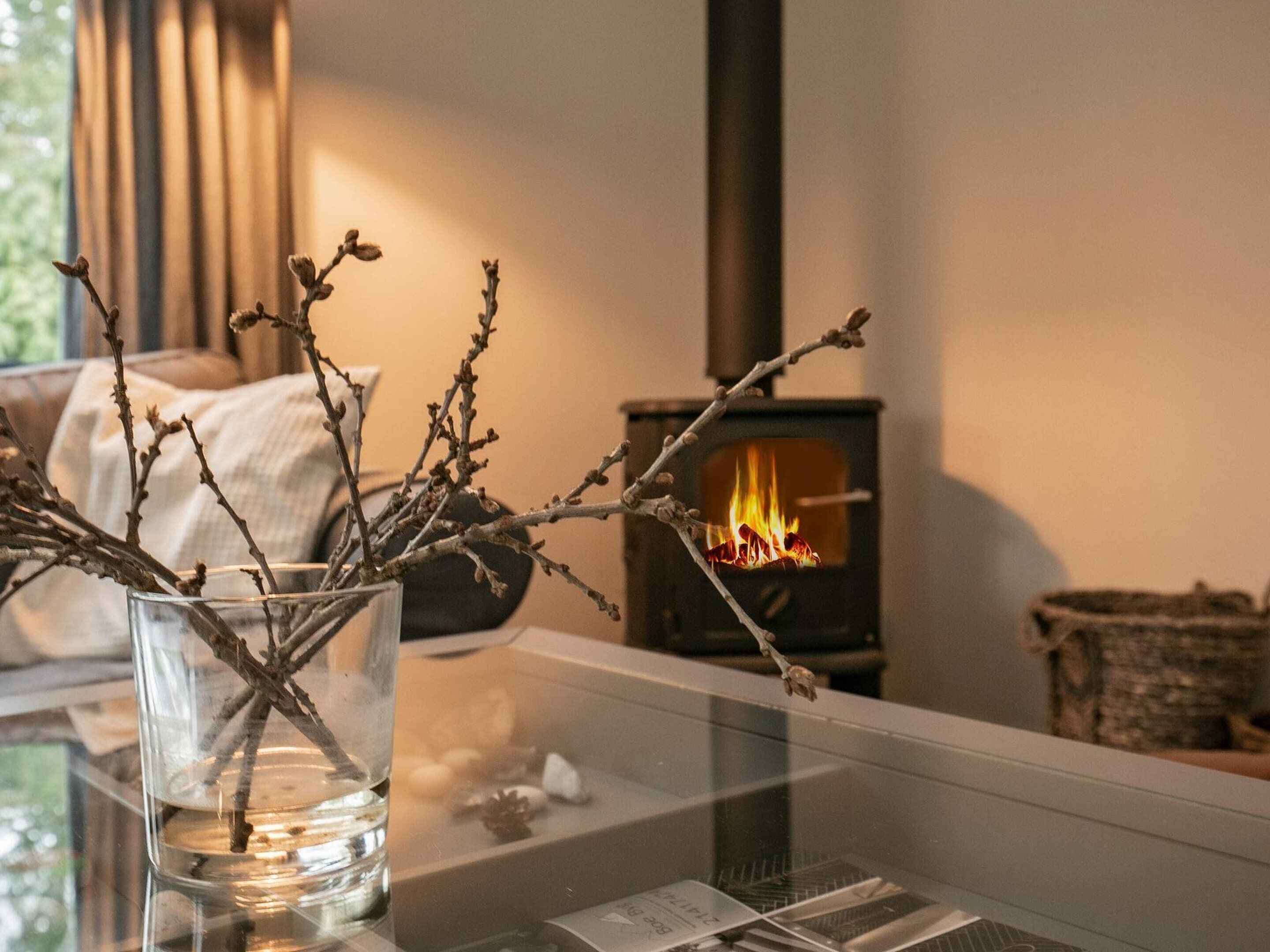 A glass vase with branches on a table near a fireplace.