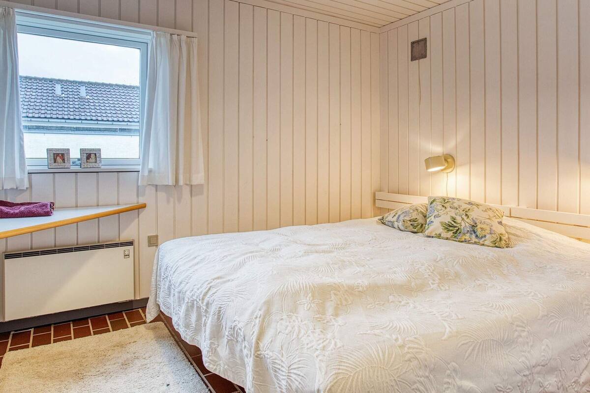 Une chambre à coucher avec un lit, une fenêtre avec des rideaux, une lampe de chevet et un radiateur.