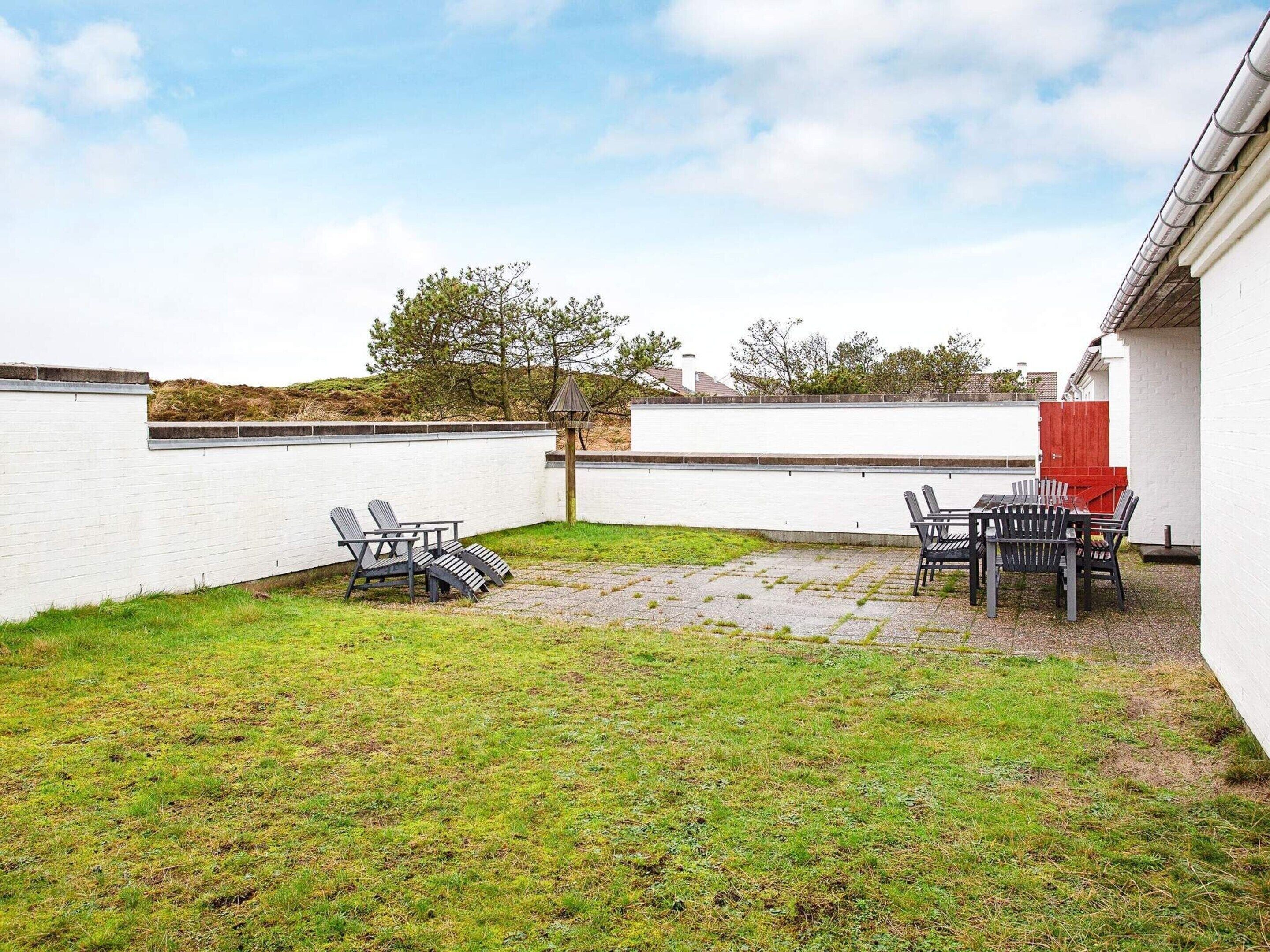 A backyard with a patio area, two sets of outdoor furniture, and a white wall.