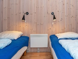 A room with two beds, a wall-mounted heater, and two wall-mounted lamps.