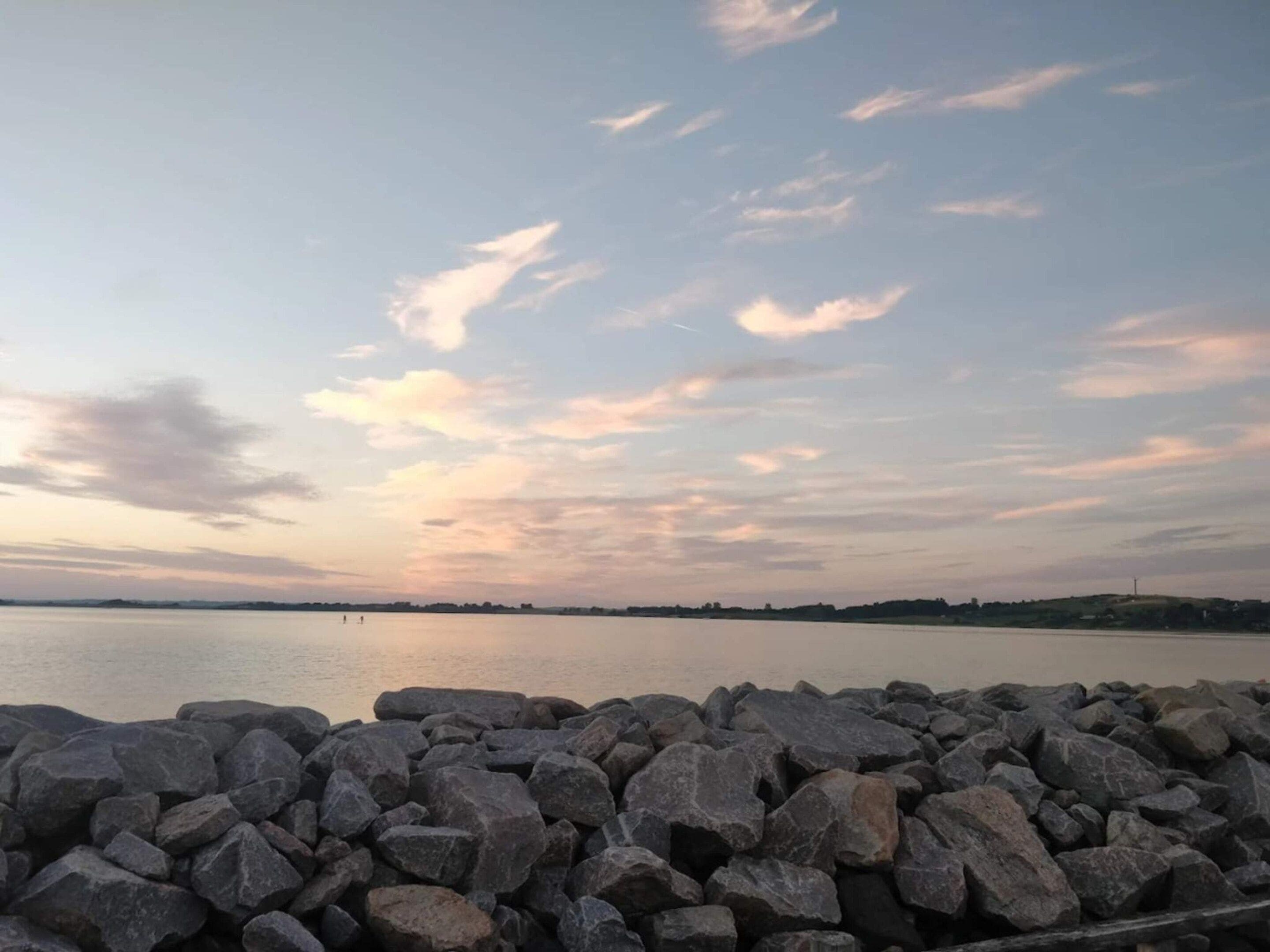 Een rotsachtige kustlijn met een rustig wateroppervlak en een verre horizon.