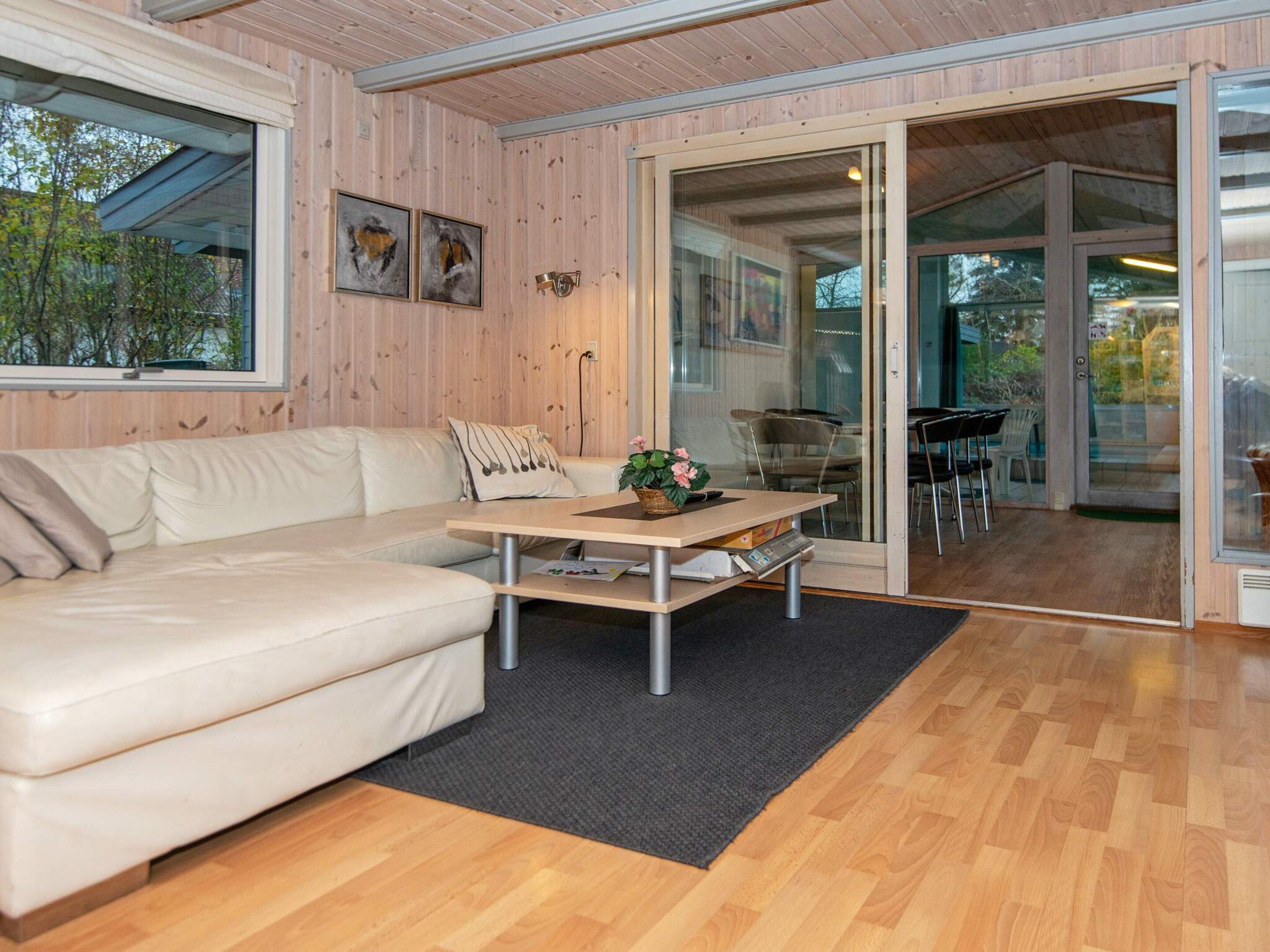 Ein modernes Interieur mit einer Couch, einem Tisch mit einem Blumenkorb und Blick durch Glastüren auf einen Außenbereich mit Stühlen.