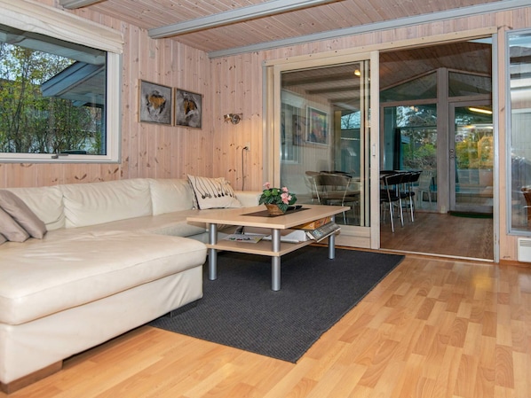 A modern interior with a sofa, a table with a basket of flowers, and a view through glass doors to an outdoor area with chairs.