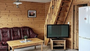 A wooden interior with a leather sofa, a wooden coffee table, a television on a stand, and a refrigerator.