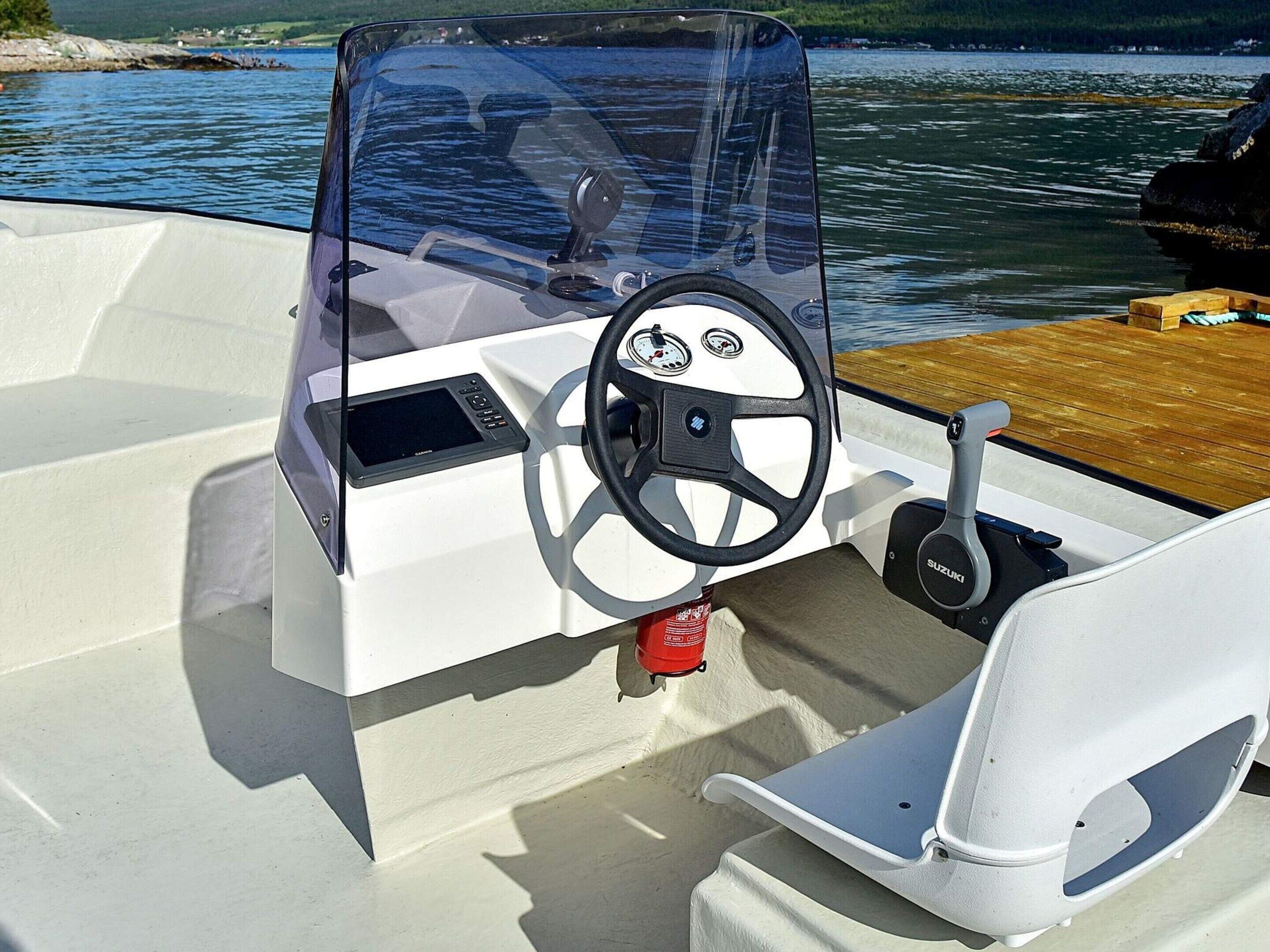 Interior de un barco con timón, panel de control y zona de estar.