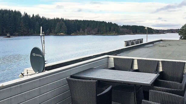 A deck with wicker furniture, a satellite dish, and a view of a lake and forest.