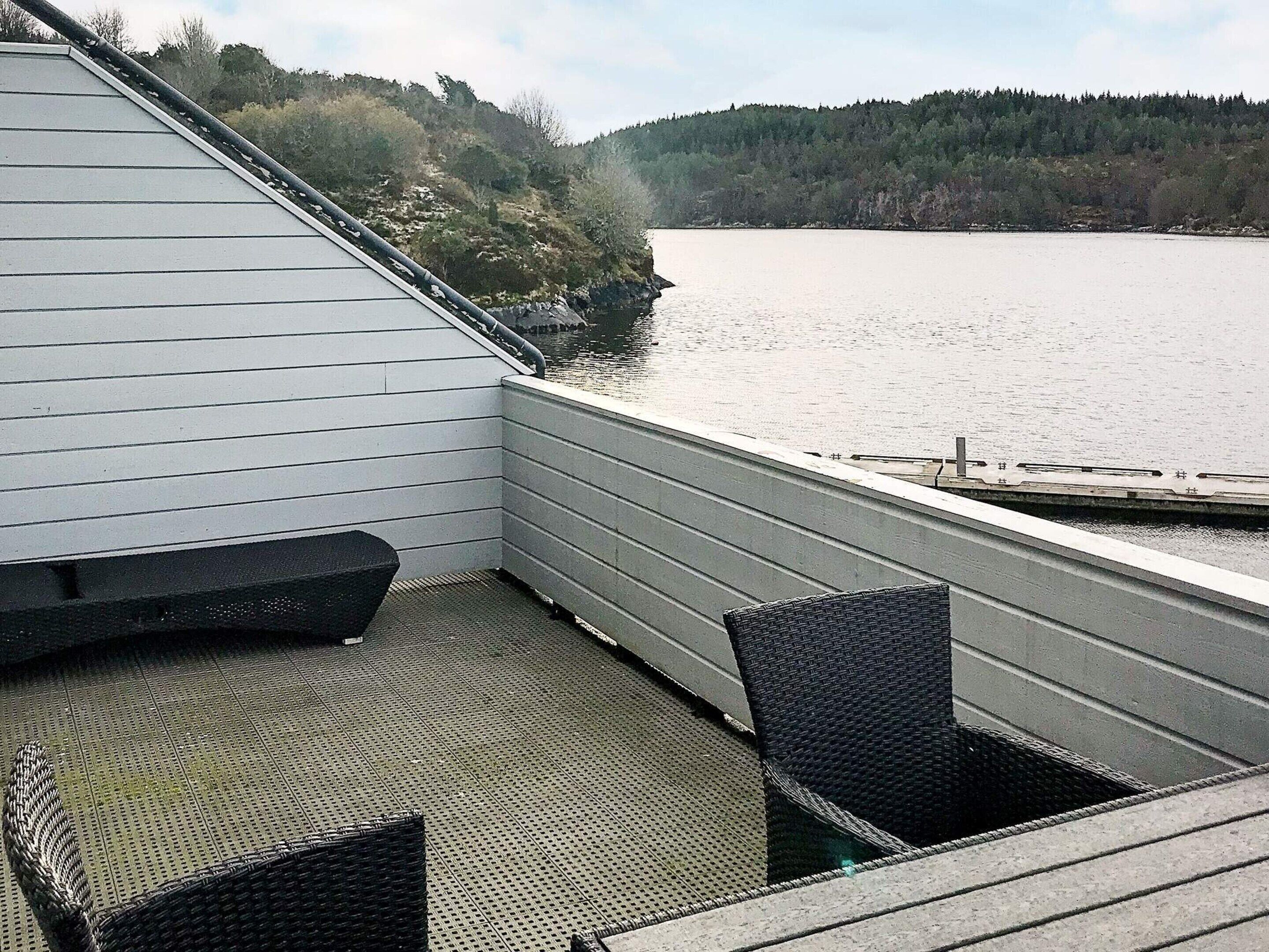 En balkong med utsikt över en sjö och en skog, en stol och ett litet bord.