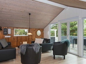 A modern living room with wooden panel walls, a ceiling fan, and a large sliding glass door leading to an outdoor area. - 6 Person Holiday Home in Romo (Rømø)