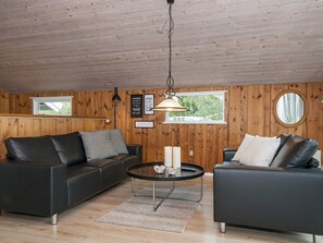 A modern living room with wooden walls, two black sofas, a round coffee table, and a hanging light fixture. - 6 Person Holiday Home in Romo (Rømø)