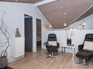 A modern room with a wooden ceiling, two black chairs, a white table, and a statue on a cabinet.