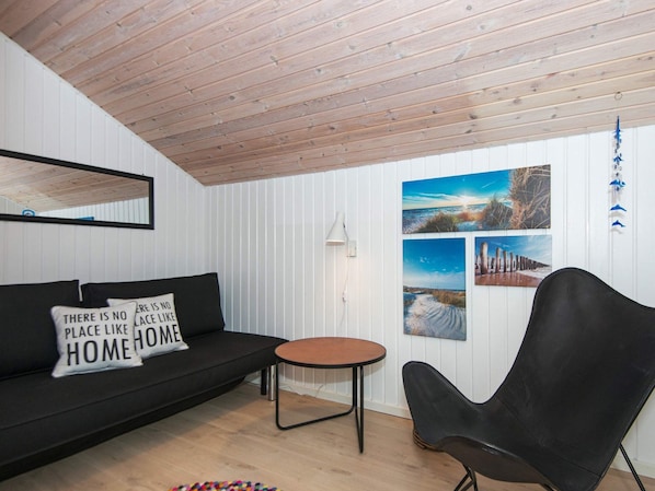 A room with a black sofa, a round table, and a black chair. There are three framed pictures on the wall.