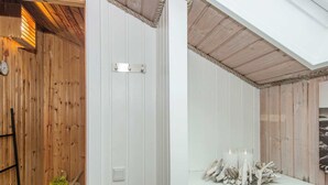 A room with wooden walls, a white door, a shelf with candles and driftwood, and a small plant on a shelf.