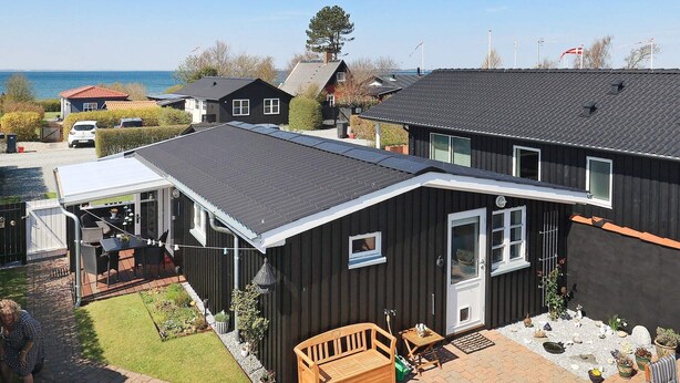 A two-story house with a covered patio, a wooden deck, and a view of the sea. - 4 Person Holiday Home in Assens (Assens)