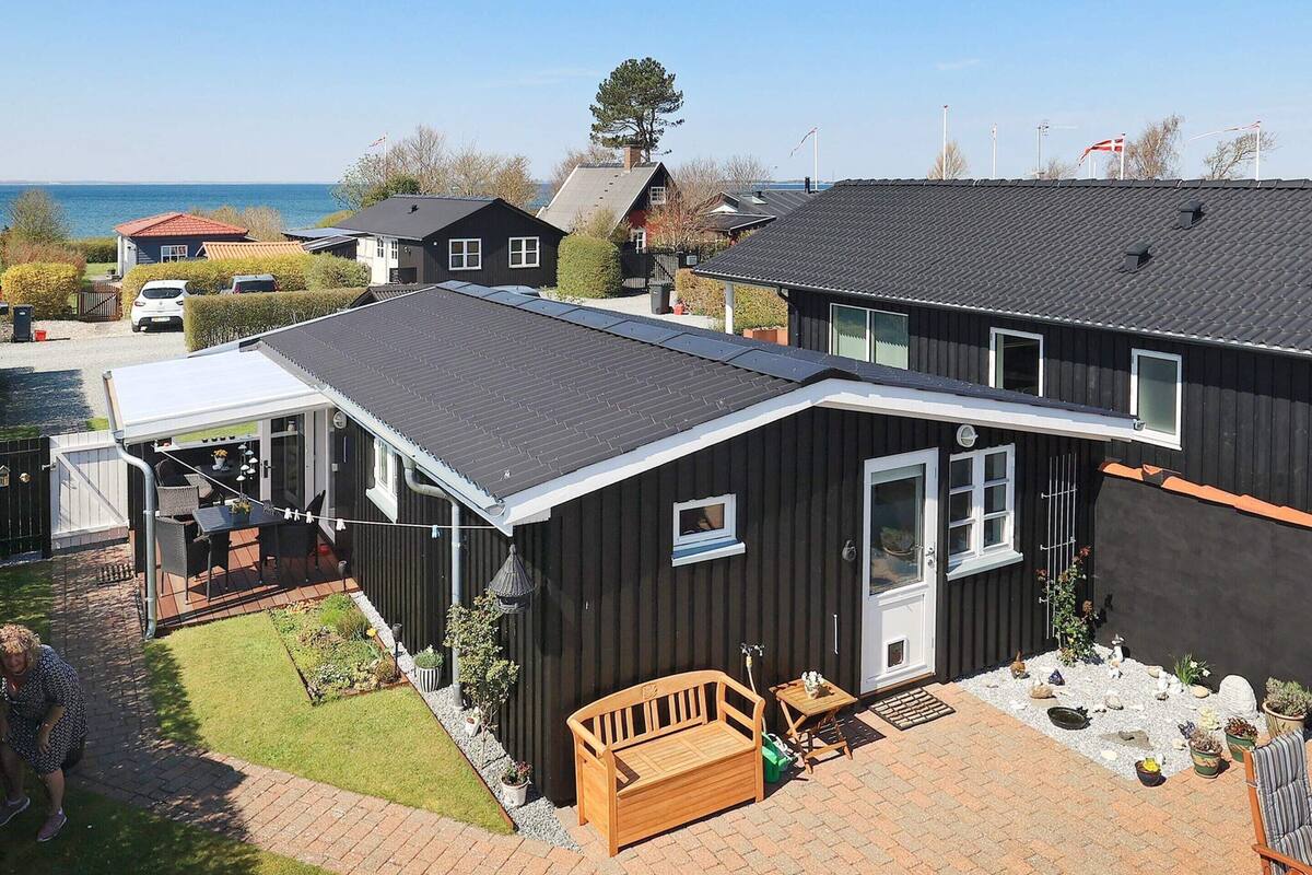 Une maison à deux étages dotée d’un patio couvert, d’une terrasse en bois et offrant une vue sur la mer.
