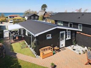 Ein zweigeschossiges Haus mit überdachter Terrasse, einer Holzterrasse und Blick aufs Meer.