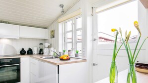 A modern kitchen with white cabinets, a black oven, a sink, and a window with a view of the outside. There are two vases with green plants on the counter. - 4 Person Holiday Home in Assens (Assens)