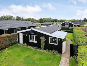A residential area with multiple houses, each featuring a distinct architectural style, surrounded by well-maintained gardens and a clear sky.