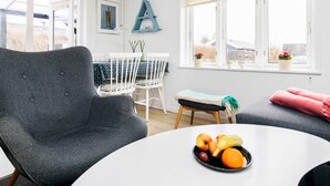 A modern living room with a grey armchair, a white round table with fruit, a small white table, and a window with a view of the outdoors. - 4 Person Holiday Home in Assens (Assens)