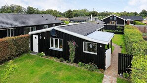A row of black houses with satellite dishes, surrounded by well-maintained gardens and a clear sky. - 4 Person Holiday Home in Assens (Assens)