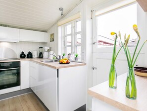 A modern kitchen with white cabinets, a built-in oven, a sink, and a window with a view of the outside. - 4 Person Holiday Home in Assens (Assens)