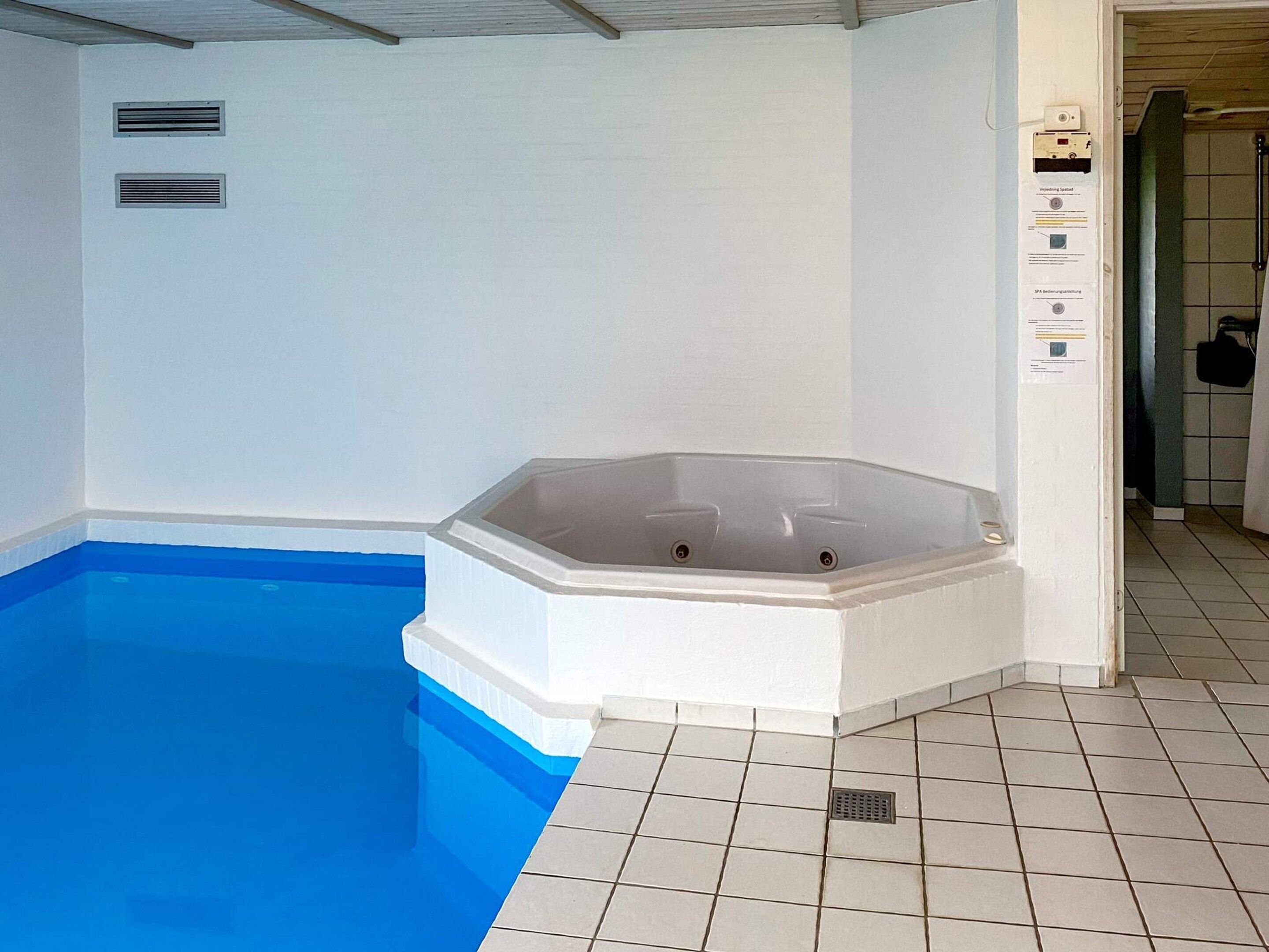 A swimming pool with a hot tub, tiled walls, and a tiled floor.