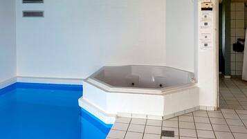 A swimming pool with a hot tub, tiled walls, and a tiled floor.