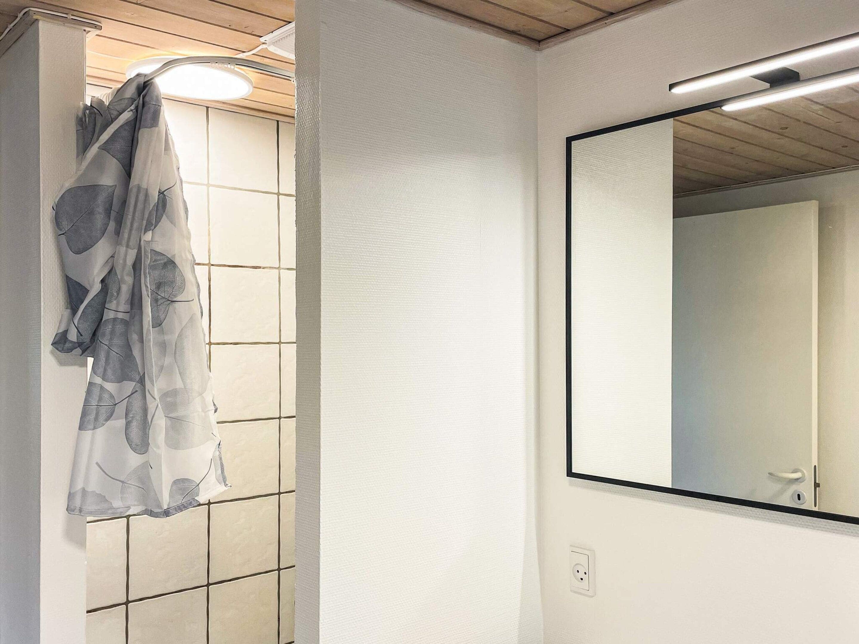 Un bagno con parete piastrellata, tenda della doccia con motivo a foglie e specchio con cornice nera.