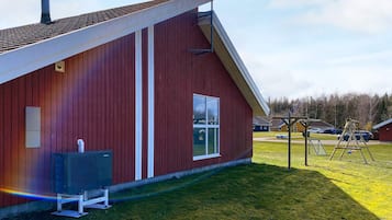 Un bâtiment rouge avec un toit en pente, une fenêtre et un petit espace extérieur équipé d’une balançoire.