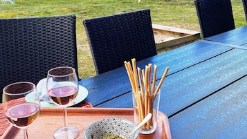 Une table bleue pour l’extérieur, avec des chaises en osier, un verre de vin et un bol de collations.