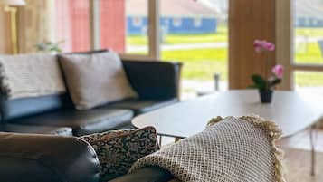 Een moderne woonkamer met een zwarte leren bank, een ronde salontafel en een groot raam met uitzicht op het landschap.